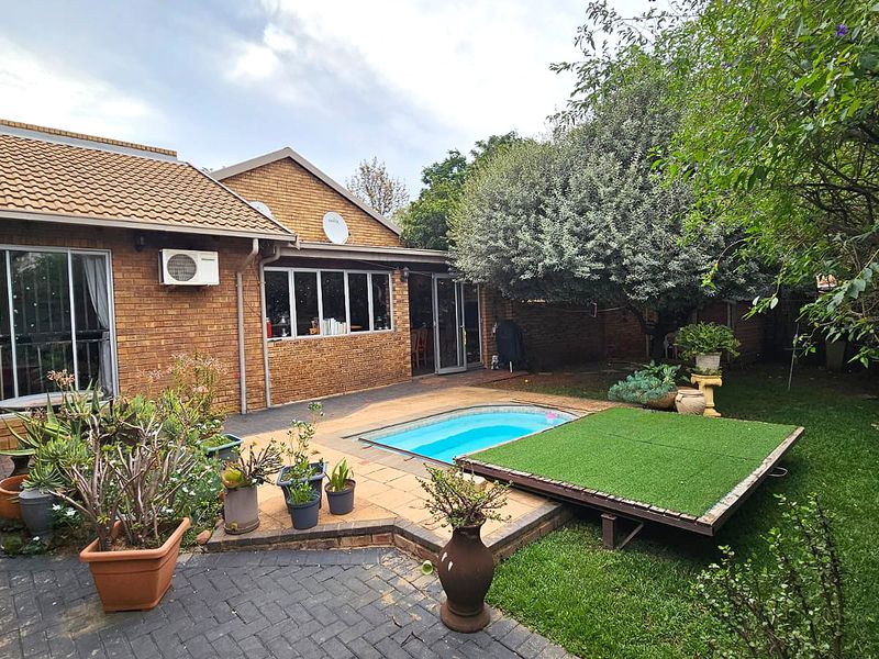 Rear exterior view of a brick duet property featuring a paved patio area, a small swimming pool, and established garden landscaping.