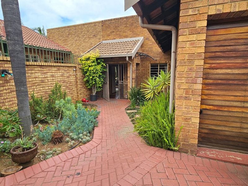 Front entrance area featuring a paved walkway, face brick exterior, and a wooden garage door, surrounded by established garden beds.