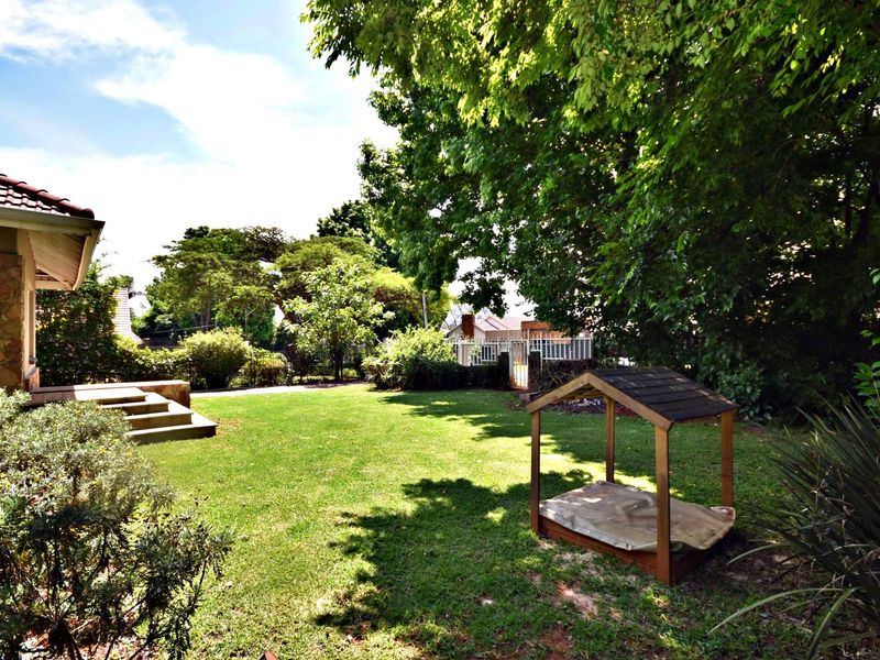 A spacious, well-maintained garden featuring a lush lawn, mature trees, and concrete steps leading to the rear of the house.