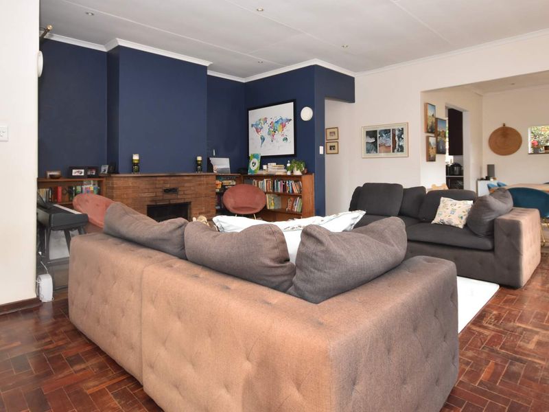 Spacious open-plan living and dining area featuring a classic brick fireplace, rich parquet flooring, and direct access to the outdoor patio.