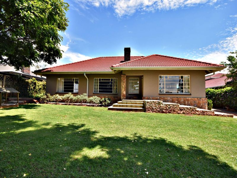 A well-maintained single-story house featuring a terracotta tile roof, stone cladding accents, and a spacious front lawn with mature trees.