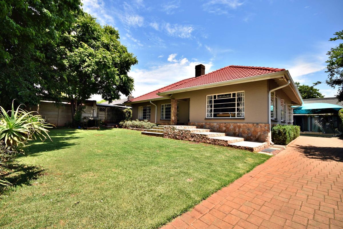 A well-maintained rear exterior view of the house featuring a tiled roof, stone cladding accents, and a spacious lawn with a brick paved driveway.