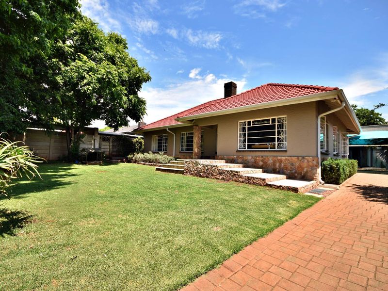 A well-maintained rear exterior view of the house featuring a tiled roof, stone cladding accents, and a spacious lawn with a brick paved driveway.