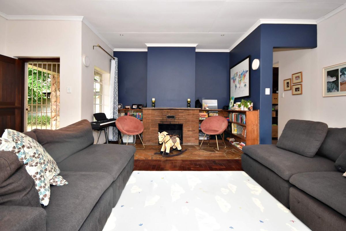 A cozy living room featuring a prominent brick fireplace, parquet flooring, and built-in shelving, accented by a bold navy feature wall.