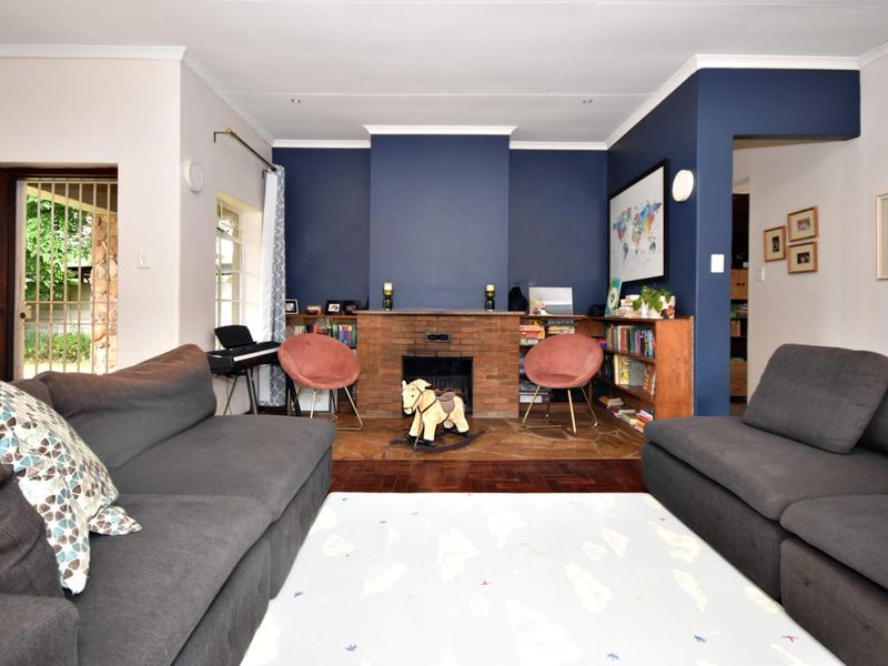 A cozy living room featuring a prominent brick fireplace, parquet flooring, and built-in shelving, accented by a bold navy feature wall.