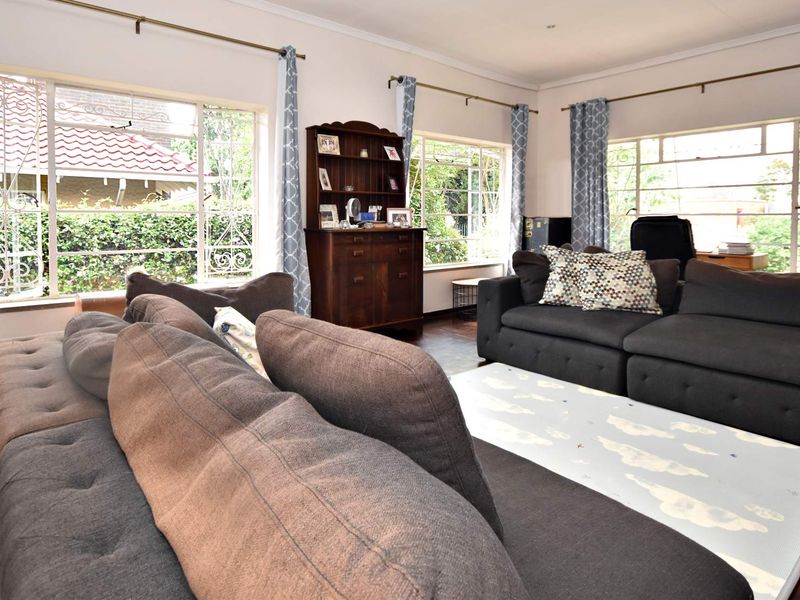 A spacious living room featuring classic parquet flooring and large windows that provide ample natural light and views of the garden.