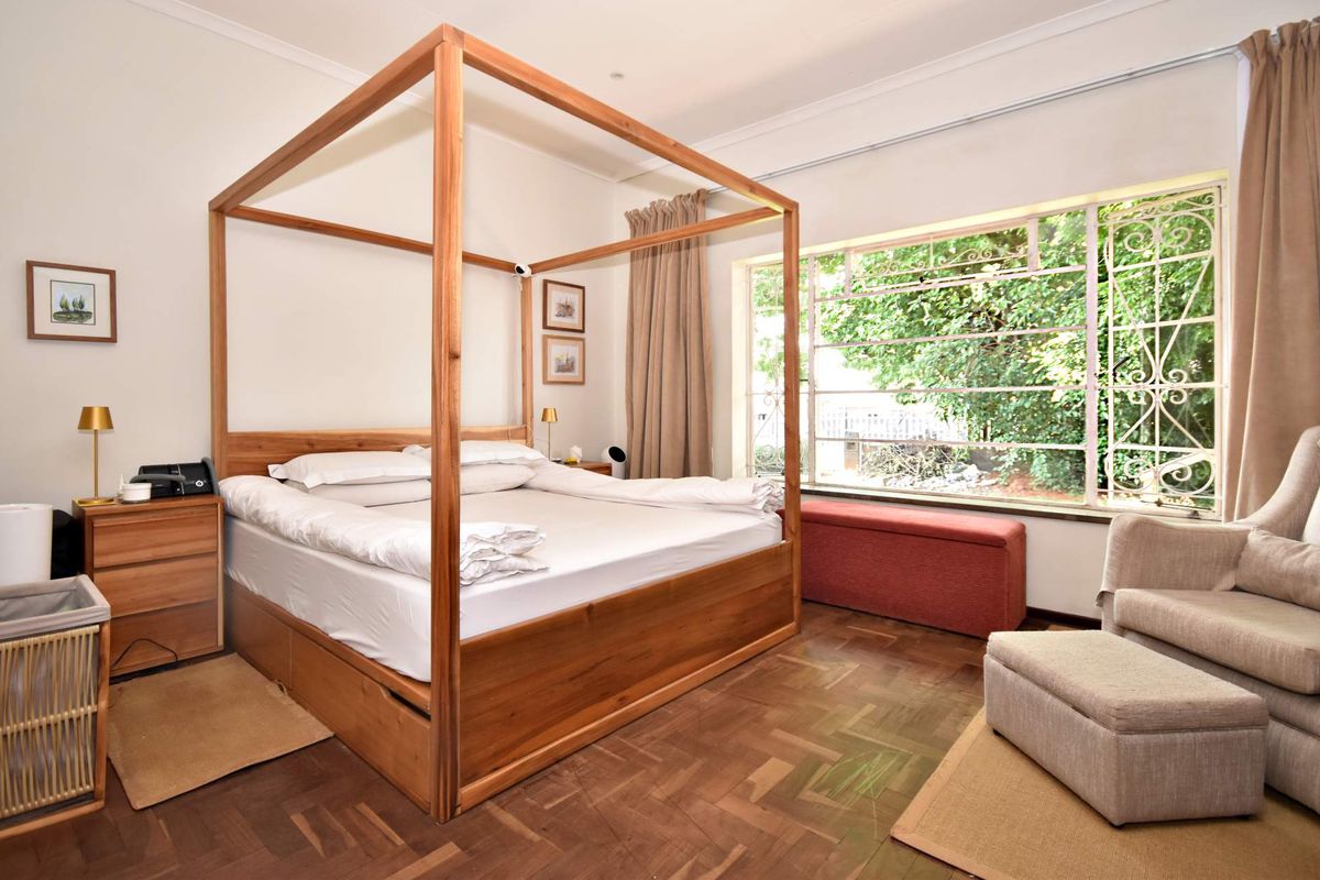 A well-lit bedroom featuring classic parquet flooring, large windows with security bars, and neutral wall finishes.
