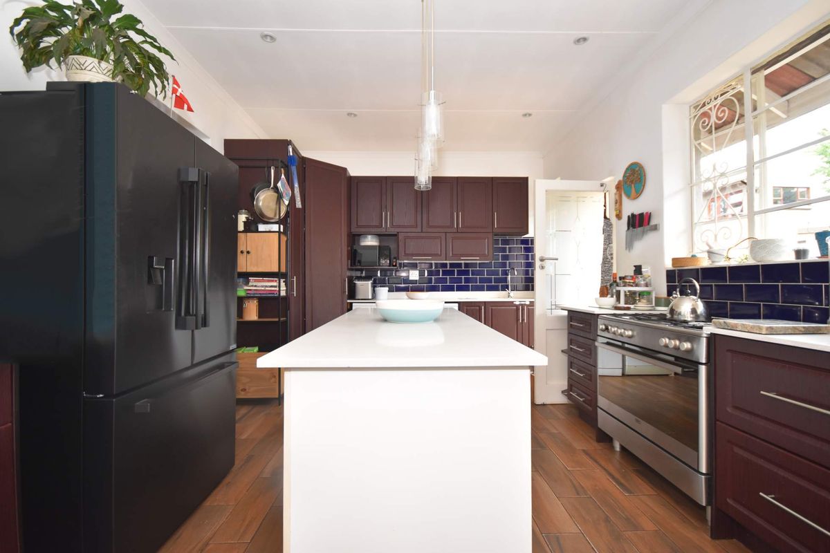 A well-appointed kitchen featuring dark wood cabinetry, a central island with a white quartz countertop, and a striking blue subway tile backsplash.