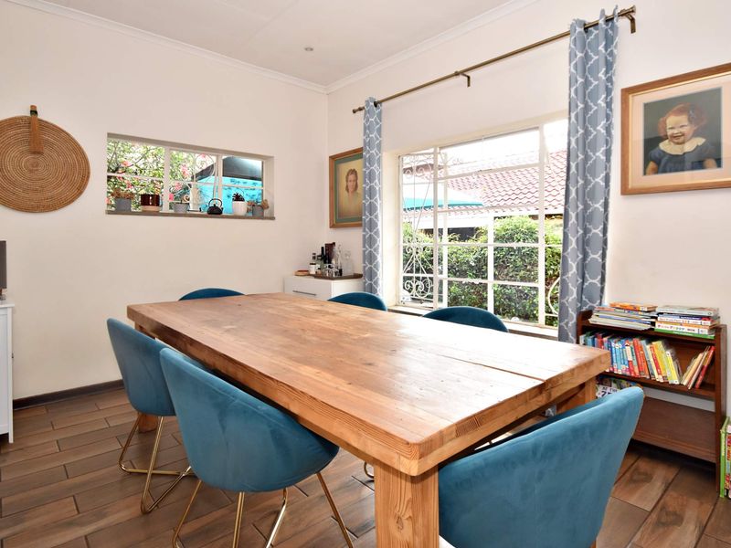 A bright dining room featuring tiled flooring, large windows with security bars, and coved ceiling details, providing a comfortable space for family meals.