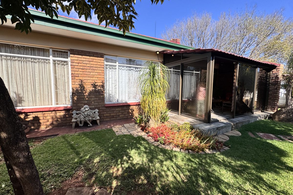 Rear view of the townhouse featuring a brick facade, an enclosed patio area, and a well-maintained garden with paved pathways.