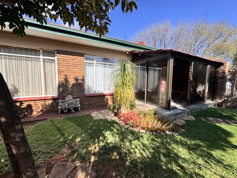 Rear view of the townhouse featuring a brick facade, an enclosed patio area, and a well-maintained garden with paved pathways.