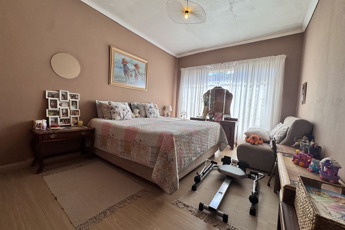 A spacious bedroom featuring laminate flooring and large windows with curtains, currently showing signs of ceiling water damage.
