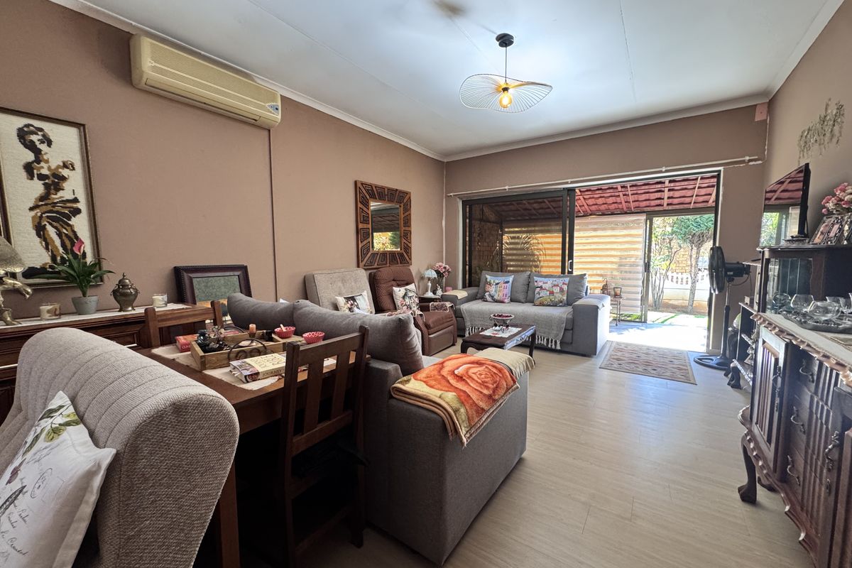 A comfortable living room featuring laminate flooring, a wall-mounted air conditioning unit, and large sliding glass doors providing direct access to the outdoor patio area.