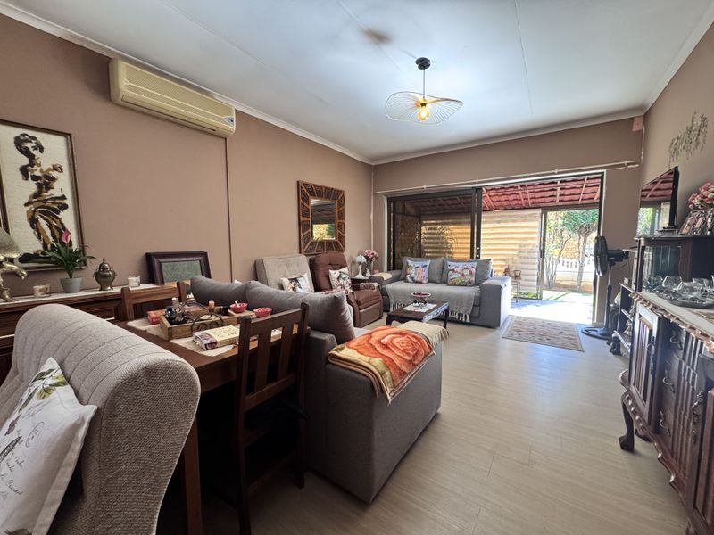A comfortable living room featuring laminate flooring, a wall-mounted air conditioning unit, and large sliding glass doors providing direct access to the outdoor patio area.