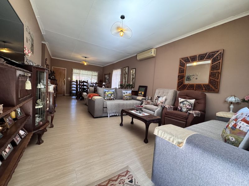 Spacious open-plan living and dining area featuring light-toned laminate flooring, neutral wall finishes, and a wall-mounted air conditioning unit.