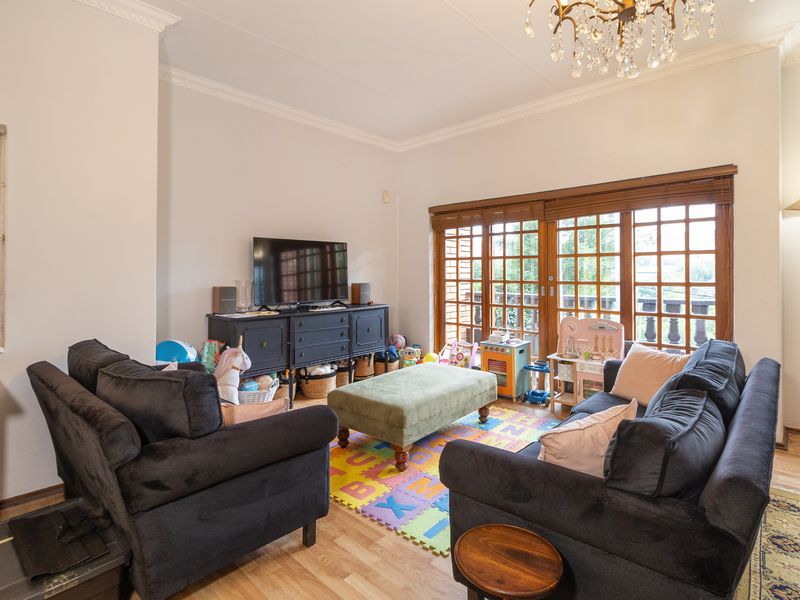 A well-lit living room featuring hardwood flooring, crown molding, a crystal chandelier, and timber-framed sliding doors leading to an outdoor area.