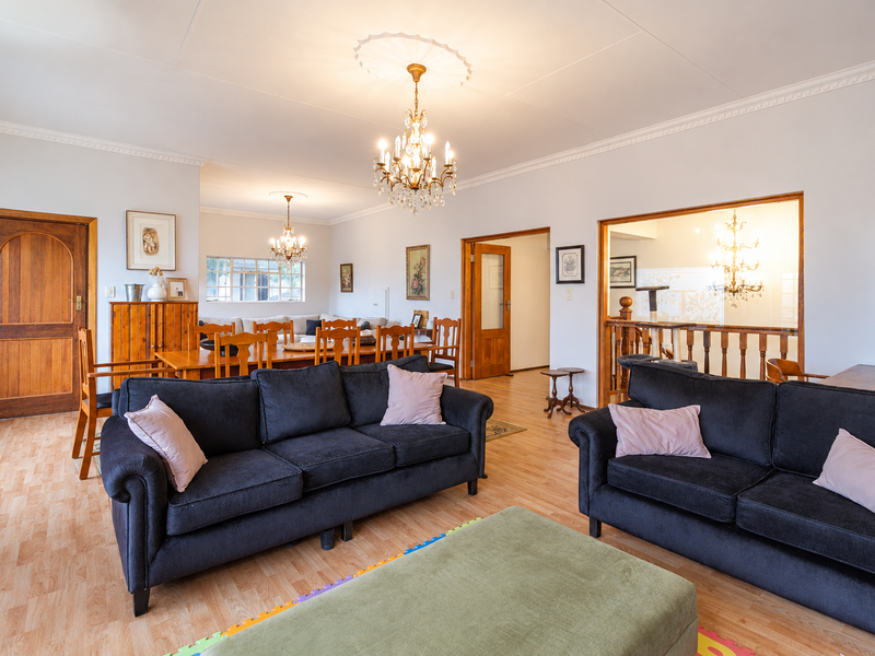 Spacious open-plan living and dining area featuring laminate flooring, classic crown molding, and elegant crystal chandeliers, creating a warm and inviting atmosphere.