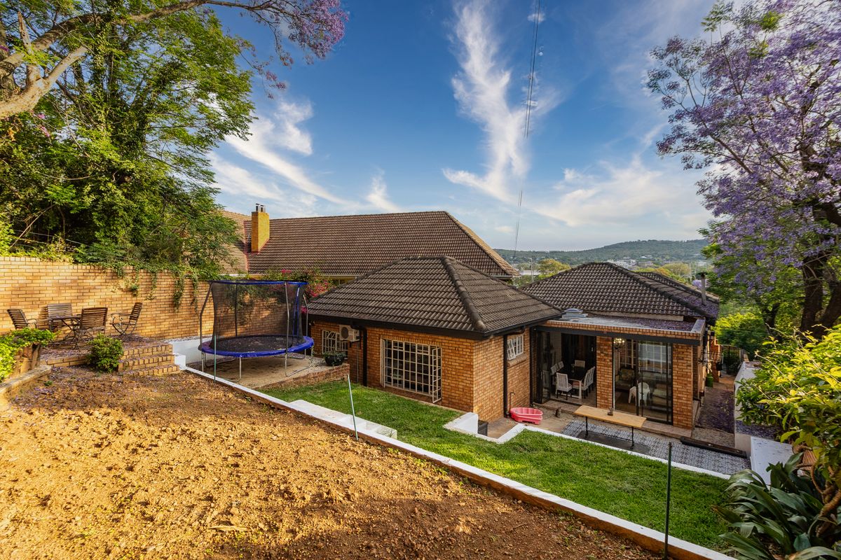 Rear view of the property featuring a brick facade, tiled roof, covered patio area, and a multi-level garden with retaining walls.
