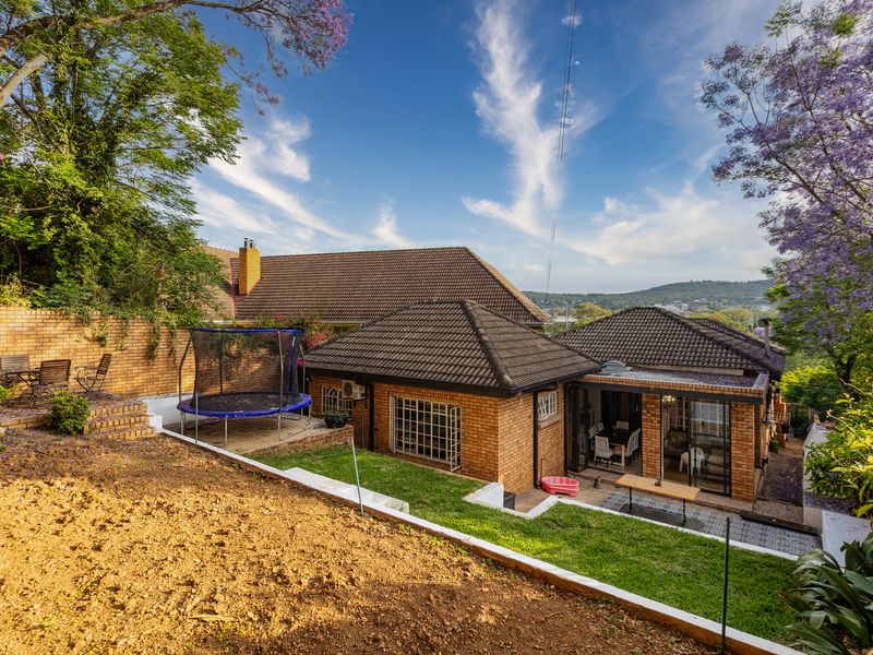 Rear view of the property featuring a brick facade, tiled roof, covered patio area, and a multi-level garden with retaining walls.