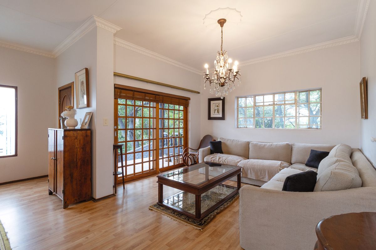 A bright living room featuring laminate flooring, crown molding, a classic crystal chandelier, and wooden sliding doors leading to an outdoor area.