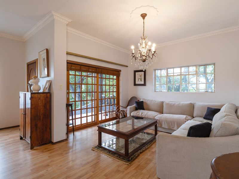 A bright living room featuring laminate flooring, crown molding, a classic crystal chandelier, and wooden sliding doors leading to an outdoor area.