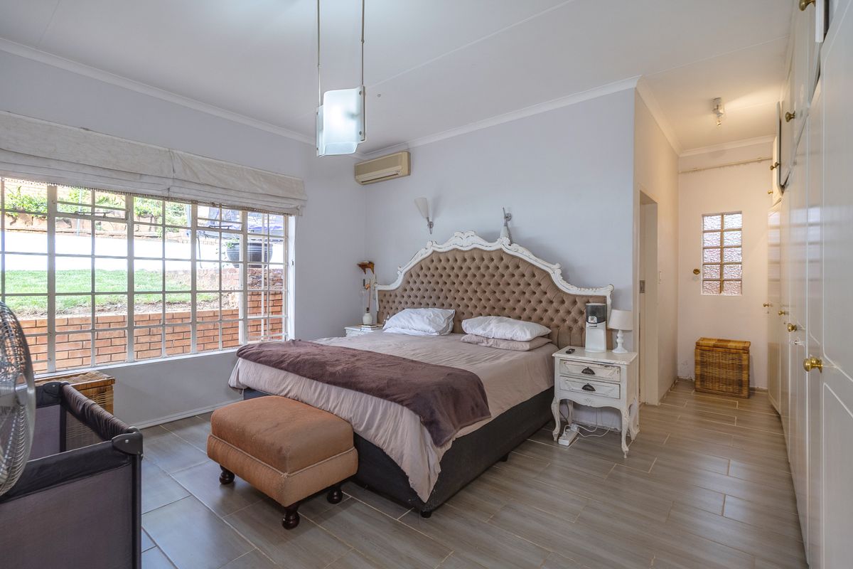 A spacious bedroom featuring tiled flooring, built-in cupboards, and an air conditioning unit, with large windows providing natural light.