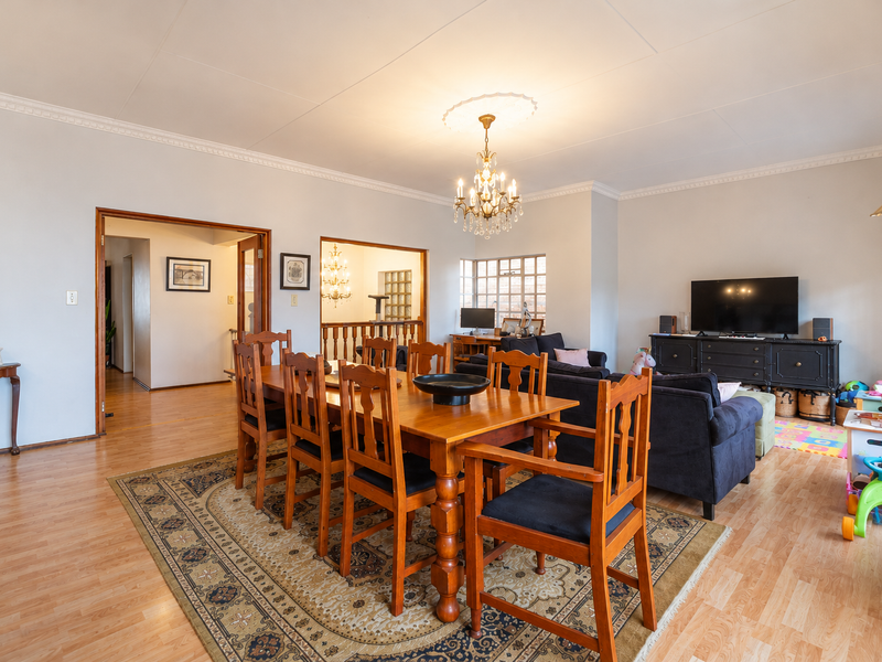 Spacious open-plan living and dining area featuring laminate flooring, classic crown molding, and a decorative ceiling rose with a chandelier.