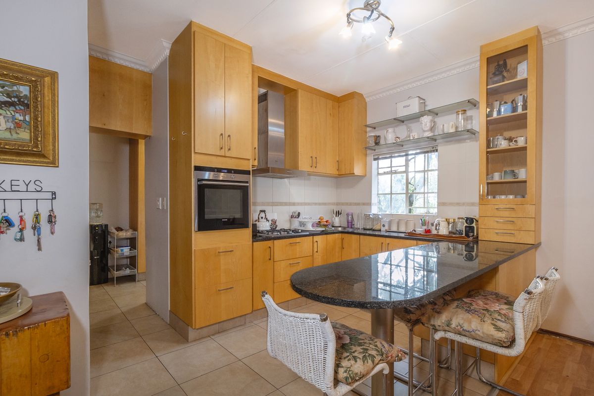 Functional kitchen featuring light wood cabinetry, granite countertops with an integrated breakfast bar, built-in oven, gas hob, and tiled flooring.