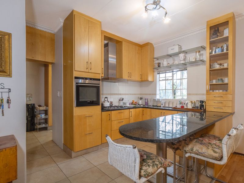 Functional kitchen featuring light wood cabinetry, granite countertops with an integrated breakfast bar, built-in oven, gas hob, and tiled flooring.