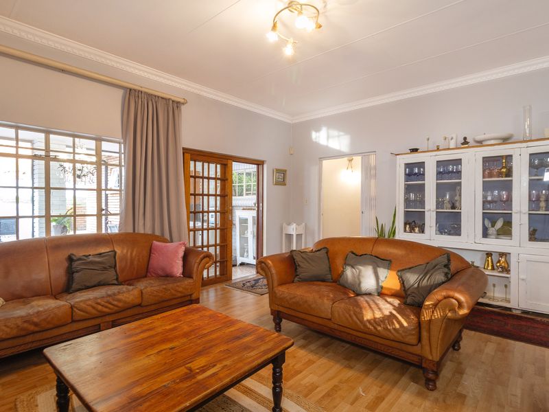 A spacious living room featuring laminate flooring, decorative ceiling cornices, and a built-in display cabinet, with access to an adjoining room via sliding doors.