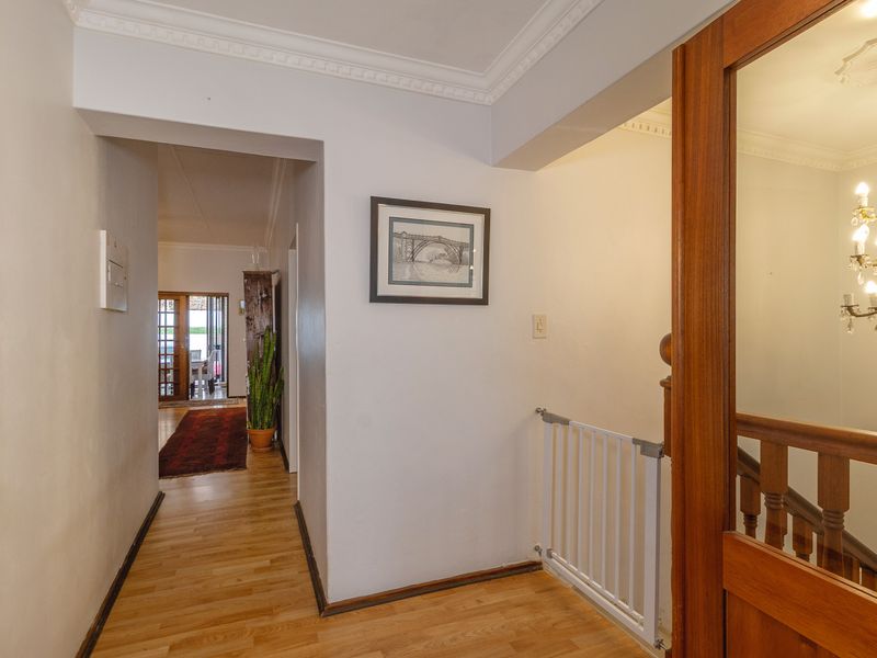 A bright hallway featuring wooden flooring, crown molding, and a wooden staircase railing, leading through to an open living area.