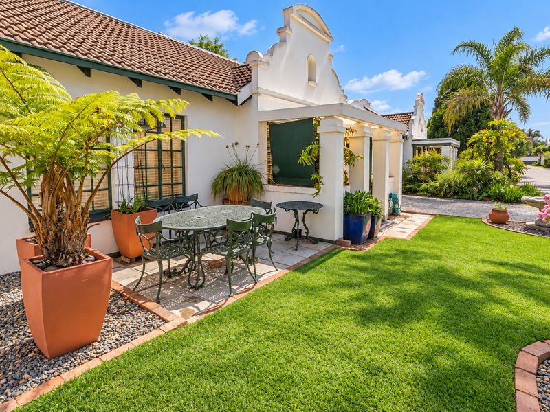 A well-maintained rear exterior view featuring a paved patio area under a pergola, overlooking a lush green garden with established landscaping.