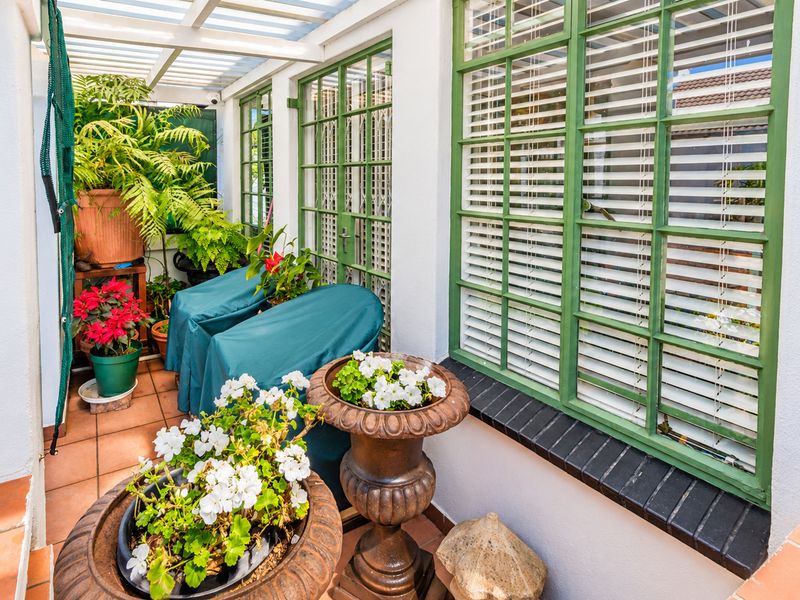 A covered patio area featuring tiled flooring, green-framed windows, and a pergola structure, providing a pleasant outdoor space for relaxation.