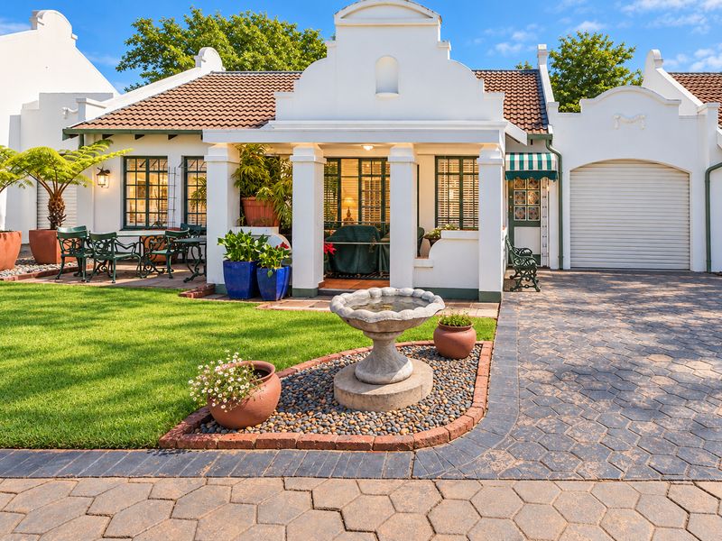 Charming Cape Dutch style retirement home featuring a well-maintained garden, paved driveway, integrated garage, and a welcoming covered patio entrance.