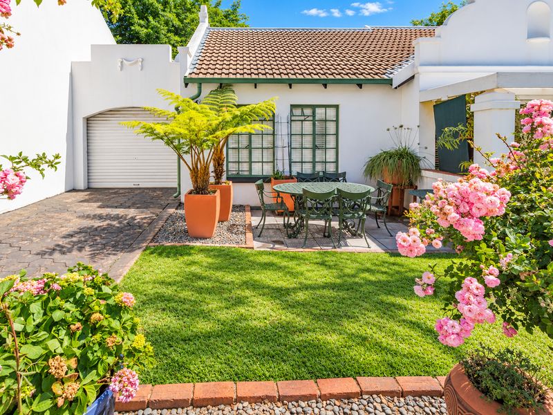 A well-maintained rear exterior view featuring a paved driveway, a garage, and a landscaped garden area with established rose bushes.