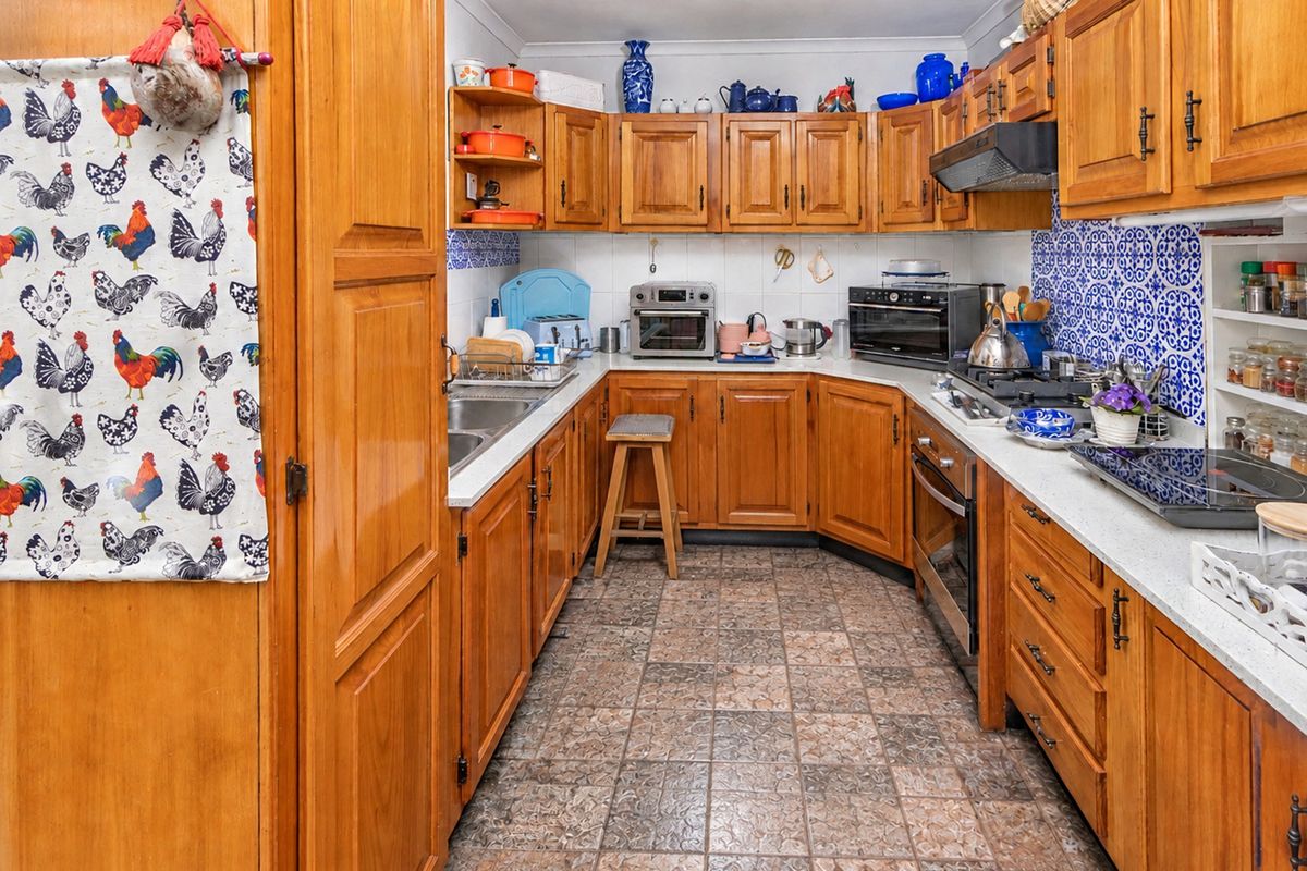 A functional kitchen featuring traditional wooden cabinetry, a built-in oven with gas hob, extractor fan, and durable tiled flooring with a decorative backsplash.