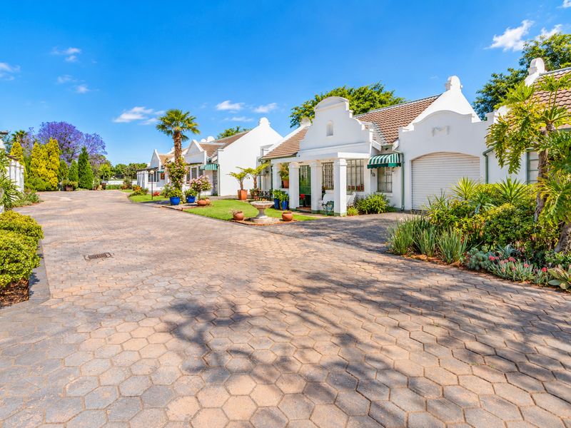 A well-maintained retirement village street view featuring paved driveways, gabled architectural details, and established garden landscaping.