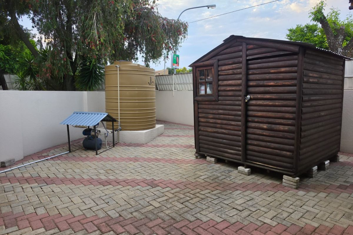 Rear courtyard area featuring a paved surface, a large water storage tank with pump, and a wooden garden shed.