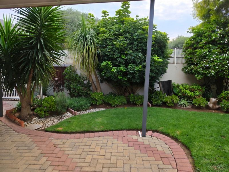 A well-maintained rear garden featuring a paved patio area, lush lawn, and established perimeter landscaping.