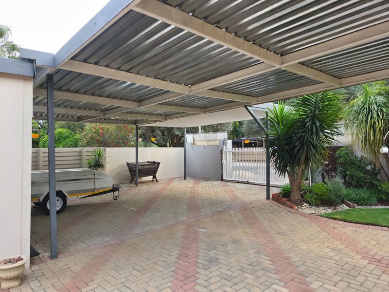 A spacious, covered carport area featuring a durable corrugated metal roof, steel support structure, and neatly paved driveway with secure perimeter walling.