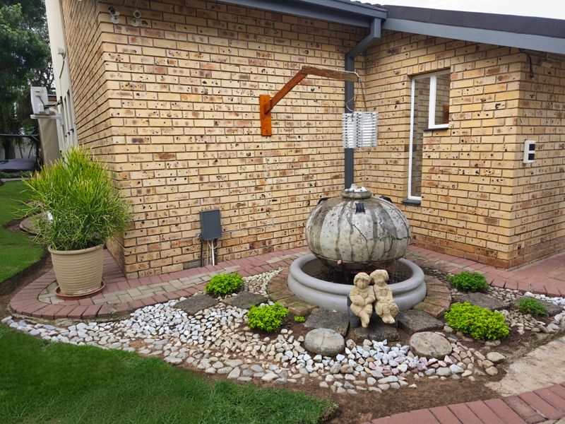 A landscaped garden area featuring a face brick exterior wall, a decorative water feature, and paved garden borders.