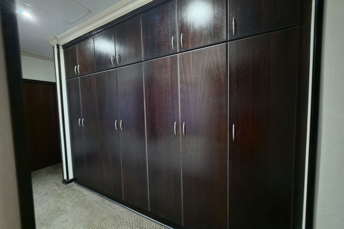 A bedroom featuring extensive floor-to-ceiling dark wood built-in cupboards and carpeted flooring.