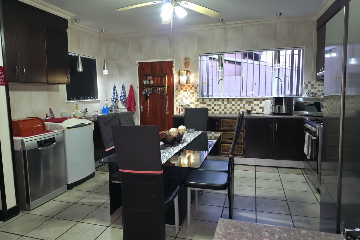 Spacious kitchen featuring dark wood cabinetry, tiled flooring, and a central dining area, offering functional workspace and integrated appliances.