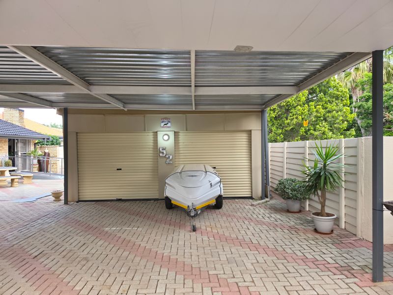 A covered carport area featuring a paved driveway and double roller shutter garage doors.