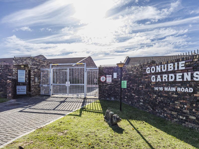 The secure gated entrance to Gonubie Gardens, featuring a brick boundary wall, paved driveway, and professional signage.