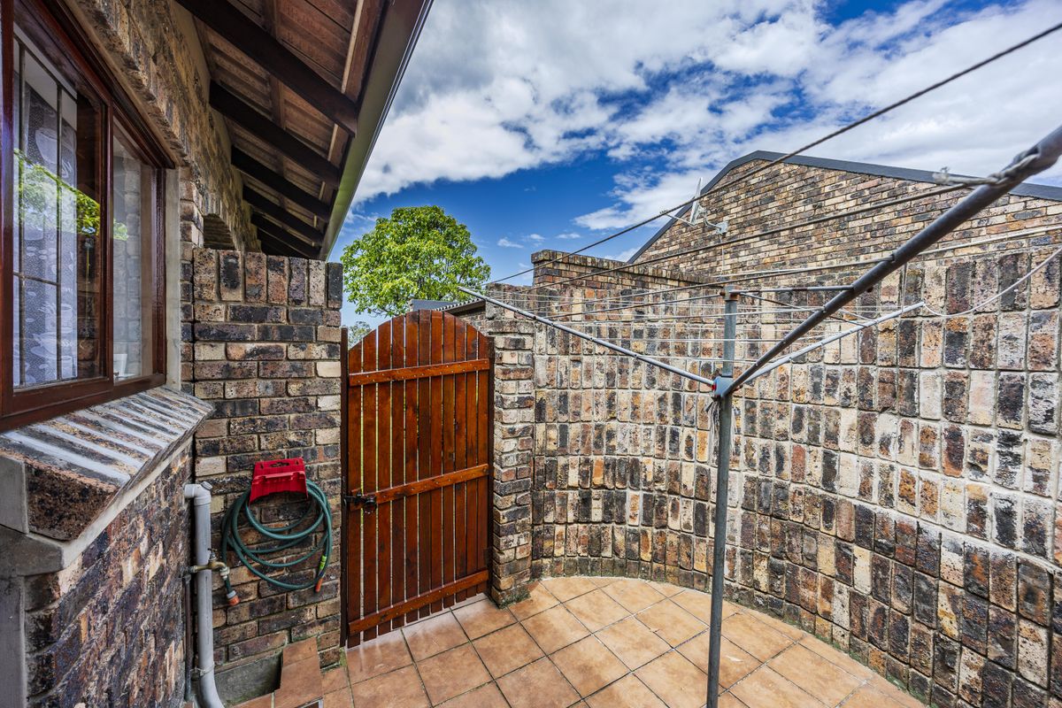 A private rear courtyard featuring face brick walls, tiled flooring, a wooden access gate, and a functional rotary clothesline.