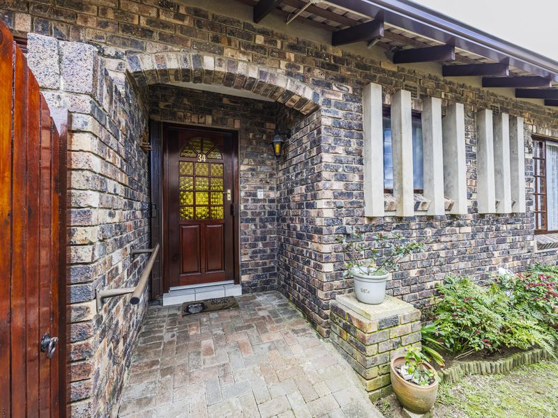 Front entrance of a townhouse featuring a classic face brick facade, arched entryway, timber door, and paved walkway with architectural concrete window detailing.