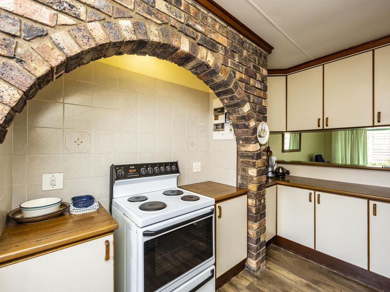 A dated kitchen featuring a distinctive brick archway, wooden countertops, and ample built-in cabinetry with a mirror splashback.