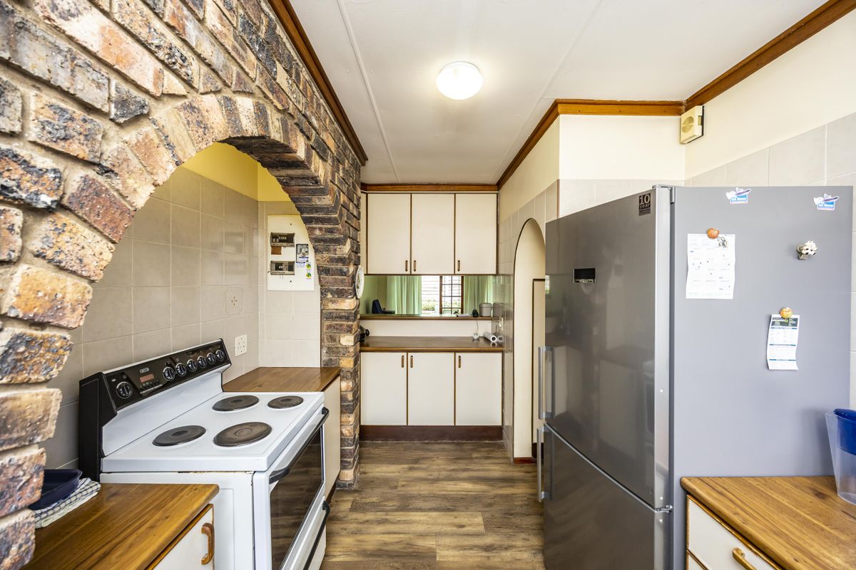 A functional kitchen featuring a distinctive brick archway, built-in cabinetry, laminate countertops, and an electric stove with a tiled backsplash.