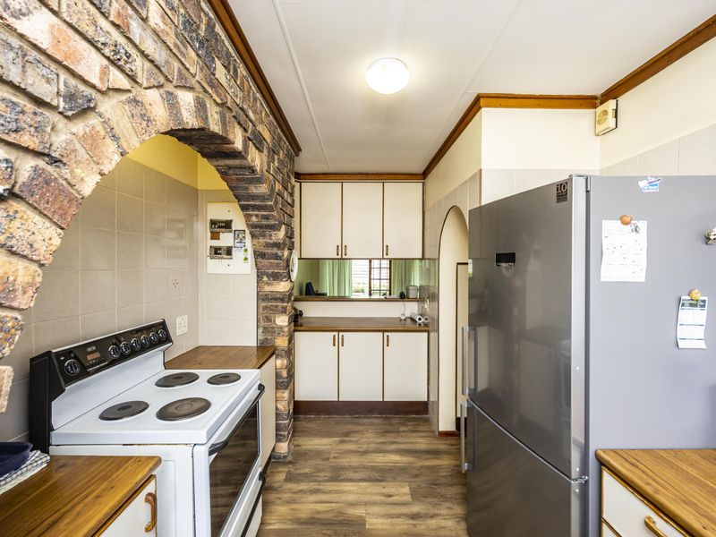 A functional kitchen featuring a distinctive brick archway, built-in cabinetry, laminate countertops, and an electric stove with a tiled backsplash.